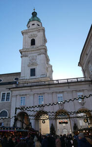 White stone church with green dome/spire. At bottom of picture, Christmas lights and Christmas market stalls