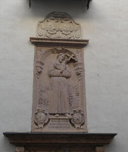 Carving of bearded monk, hands folded over chest, gazing at a crucifix