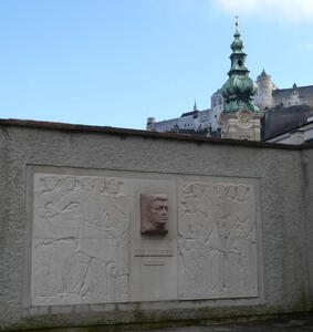Monument to Dr. Franz Rehrl; it has his bust on it. In background, a church with green dome/spire.