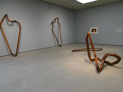Four very large irregular loops made of wood. Two are leaning against the wall, the other two on the floor. One of the loops on the floor extends in all three dimensions