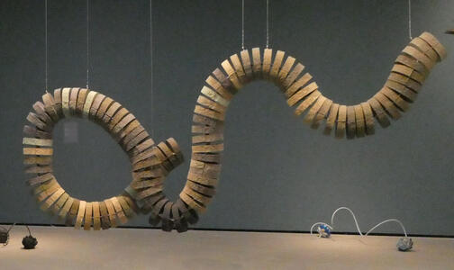 Rings of various shaded wood connected to look like a snake. The piece is suspended from the ceiling.
