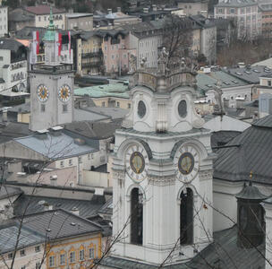 Two churches, each with their clock towers. The church on the left has red and white flags with a castle in the center