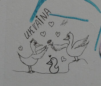 Male duck handing a flower to a female duck, with a duckling between them. In the air around them are outlines of heart symbols. It is labeled Ukraina.