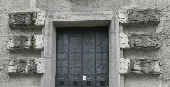 Carved angels carrying faces; one set of three on either side of a metal door