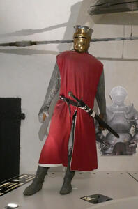 Mannequin wearing chain mail, helmet, and red robe/jacket; has two swords at waist.