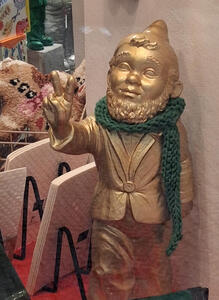 Gold gnome figurine with green scarf. Gnome is giving a peace sign.