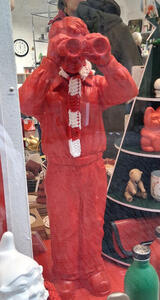 Red figurine of standing man with binoculars; figurine is wearing a red and white scarf