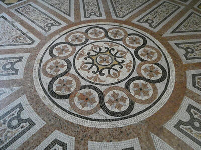 Mosaic floor tiles. An inner circle is surrounded by twelve smaller circles. Tiles are brown, black, gray, and white.