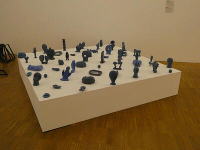 Plaform with multiple small sculptures of varying shapes, mostly in blue and black.
