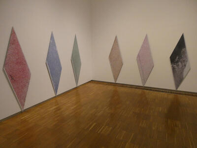 Six large diamond-shaped panels on a wall. Panels are red, blue, gren, brown, pink, and black/gray.