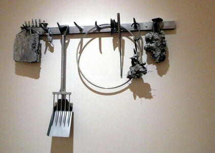 A bar with hooks. On each hook is a metal piece. Some are irregular blobs; one looks like a shovel, and one is a hoop.