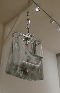 Metal mesh bag hanging from ceiling on a chain; in bag are pieces of metal