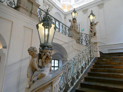 Stairway with lanterns on railing landings. Carved cherubs at the base of each lantern.