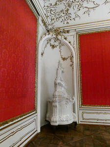 Niche at corner of two red walls. The niche is adorned with gold branches and leaves; in the niche, a statue that looks vaguely like a pagoda atop a hill.