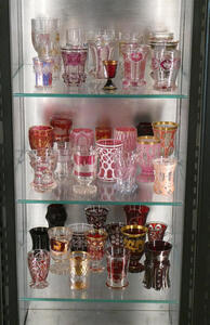 Three shelves of glassware, primarily tinted red and pink.