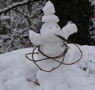 Small snowman with branch wrapped around its “waist”.