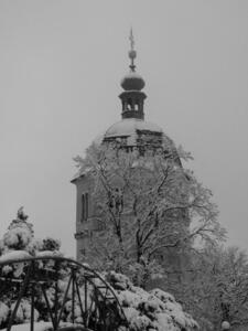Church bell tower in background, partially obscured by tree branches in foreground. At left foreground, a steel arch bridge