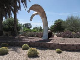 Sculpture of a plow with plowshares as curved silver arcs with spheres at end; cacti in foreground and background.