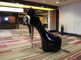 Large sculpture of high-heeled black shoe; heel is a mechanical piston-like device