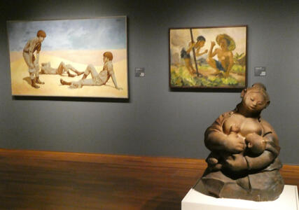 Paintings in backgorund; sculpture of woman holding infant in foreground
