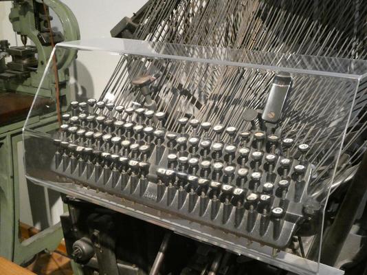 Keyboard of Linotype machine with large array of metal wires behind it.