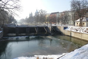 View over river from bridge; buildings in background and on side.
