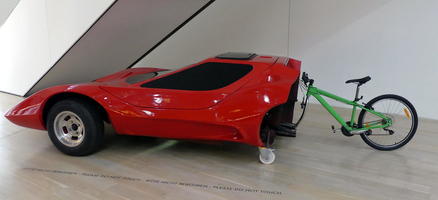 Half of red sportscar with half of bicycle on back.