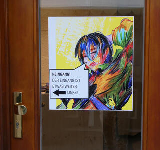 Sign with a person drawn in a crayon-abstract style. Text: NEINGANG! Der Eingang ist etwas weiter links!