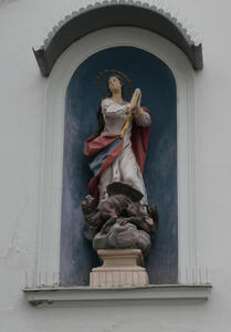 Niche with a statue of a woman in a flowing white, red, and blue dress. Her hands are folded in prayer.