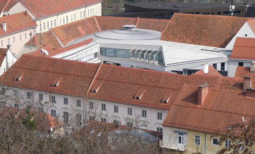 Modern building with a circular roof surrounded by old buildings with ordinary reddish-tiled roofs.