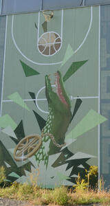 Below a basketball hoop: painting of a basketball falling into the open jaws of an alligator below.
