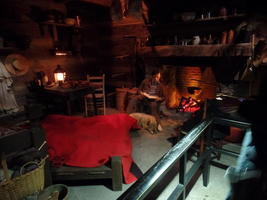 Interior log cabin; Lincoln reading in front of fireplace with dog at his feet.