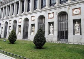 Shrubbery in foreground, building with recesses with Greek/Roman sculpture in background
