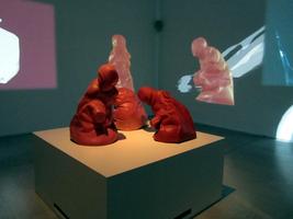 Three abstract human figures made of what appears to be red clay,hunched over