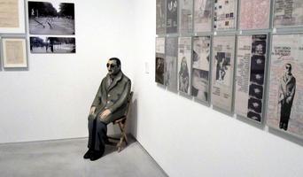 Lifelike papier maché and polychrome sculpture of man sitting in a chair in the corner of a room