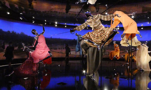 Manikins in dresses as if floatig in air; one is  holding an epee.