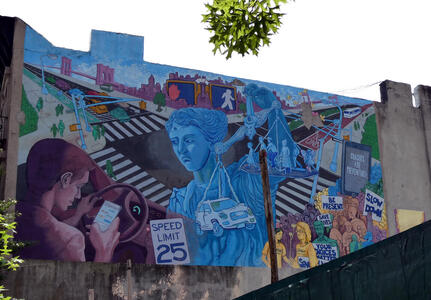 Mural of man texting while driving; Justice (holding scales with pedestrians in one pan and car in other) is scowling at man