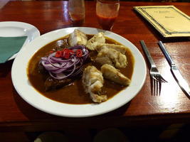Goulash with bacon dumplings on plate. Goulash has onions and red peppers on top.