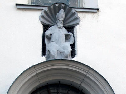 Sculpture of bishop above an entranceway. Background of sculpture is seashell-shaped.