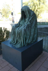 Sculpture of a seated woman. She is in a flowing robe that covers her face.