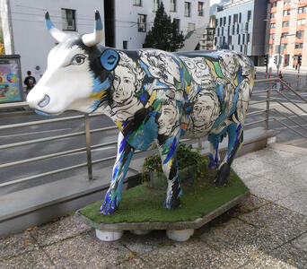 cow with white face and blue-painted lges and body. On side are drawings of people’s heads.