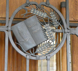 Metalwork with a book. On left page, an owl. On right page, „Wissen ist Macht“