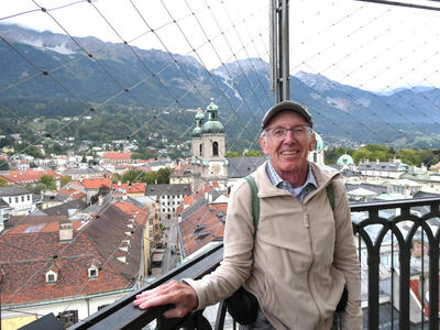 Man with glasses and English driver’s cap. In background, church and mountains