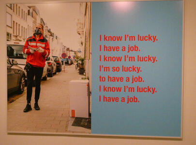 Man in red sweatshirt and black face mask. Text: I know I’m lucky. I have a job. I know I’m lucky. I’m so lucky. to have a job. I know I’m lucky. I have a job.
