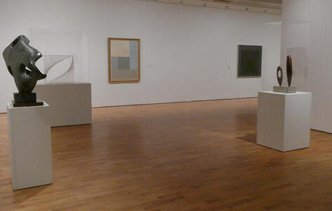 Gallery with three sculptures in foreground and two paintings in background.