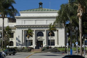 Two-story white building with greek columns and palm trees in front